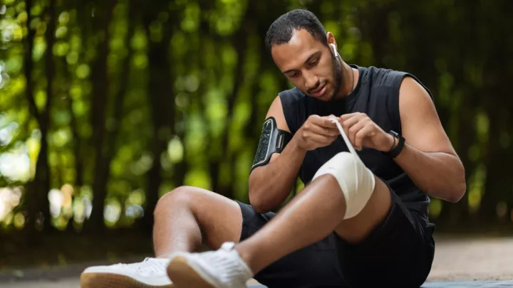Man sitting on ground, wrapping his knee